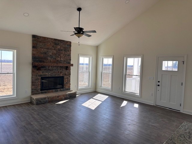 Living room featuring wood flooring, stone fireplace with mantel, ceiling fan, and large window letting in natural light