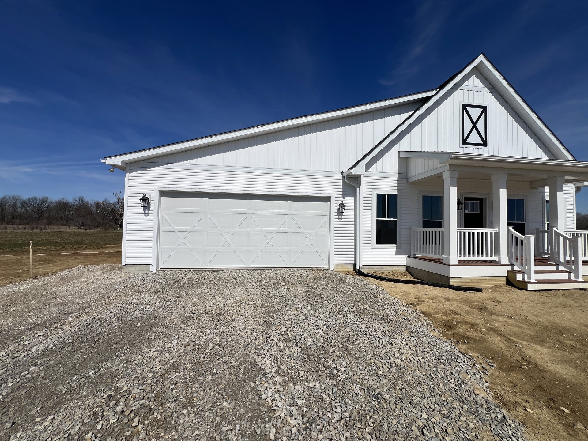 White two-story house with white siding, attached garage with white paneled door, white-framed windows, gray shingle roof, gravel driveway, and cloudy sky overhead