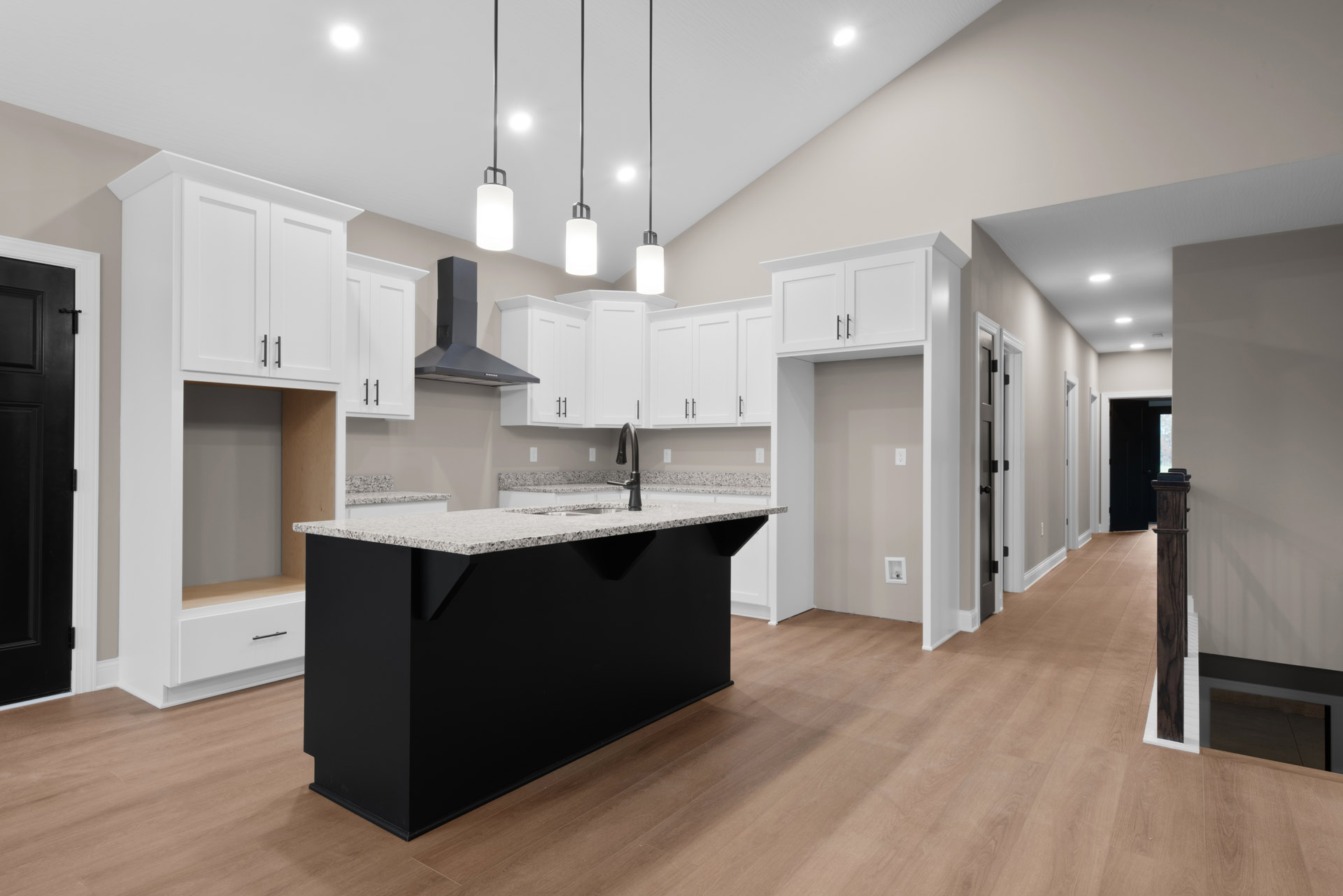 Kitchen featuring a black island with matching countertop and faucet, surrounded by white cabinets, light wood flooring, and a white pendant light with black metal frame.