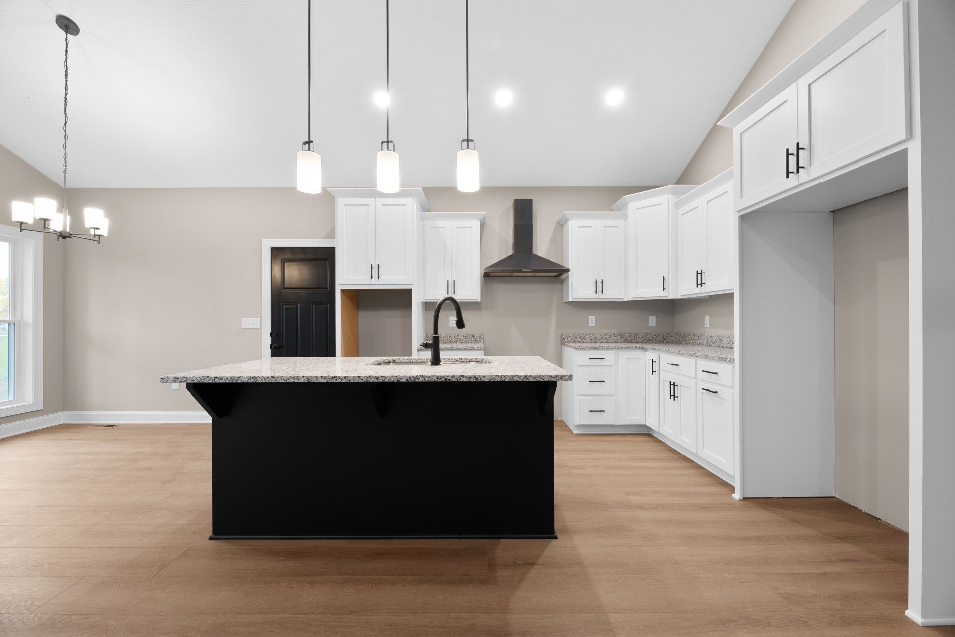 Kitchen featuring a black island with matching countertop, white cabinetry, arched window with pendant light, tile flooring, and stainless steel sink.