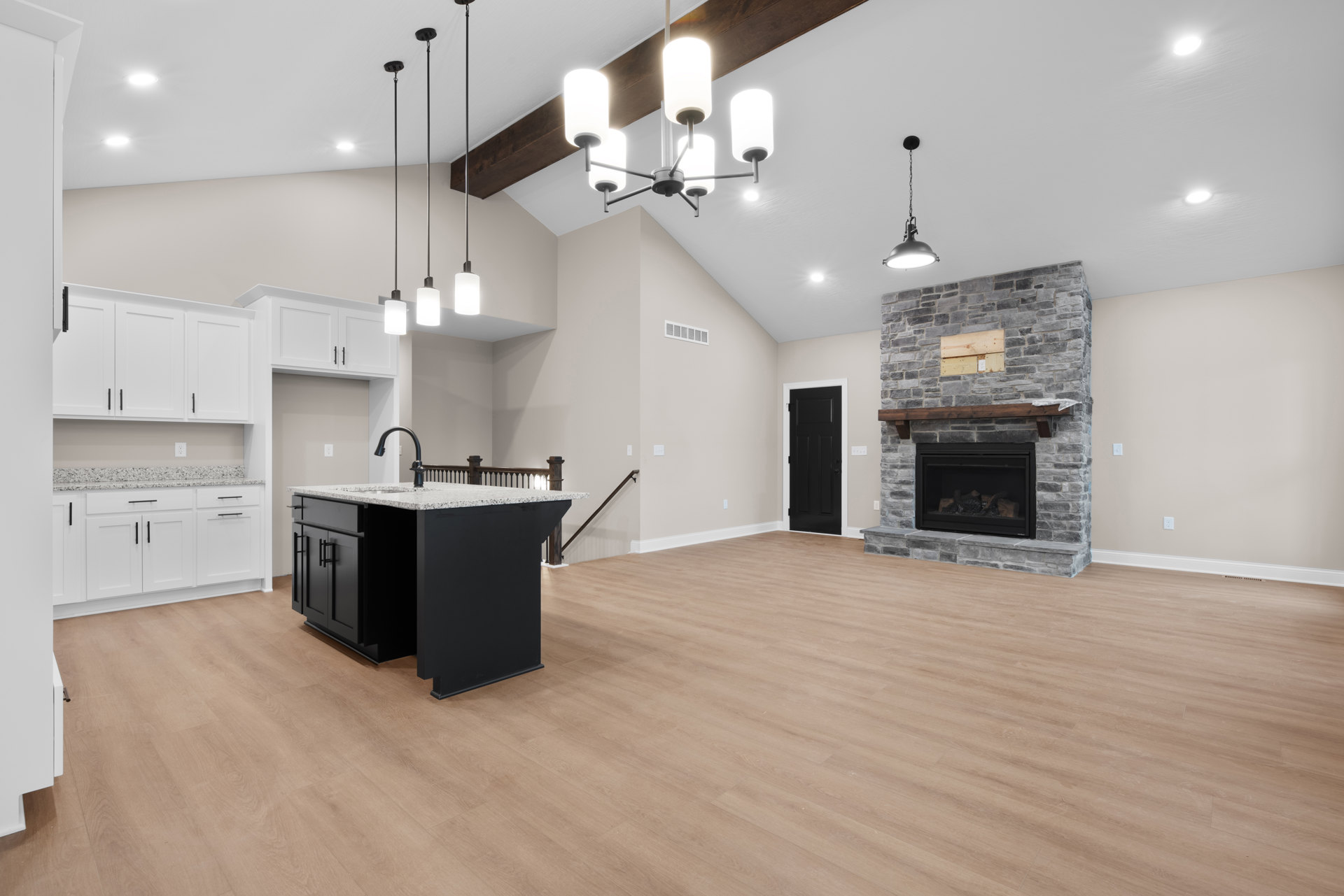 Spacious open floor plan featuring a black kitchen island with sink, hardwood flooring, fireplace with stacked wood, black door with white trim, and black ceiling chain.