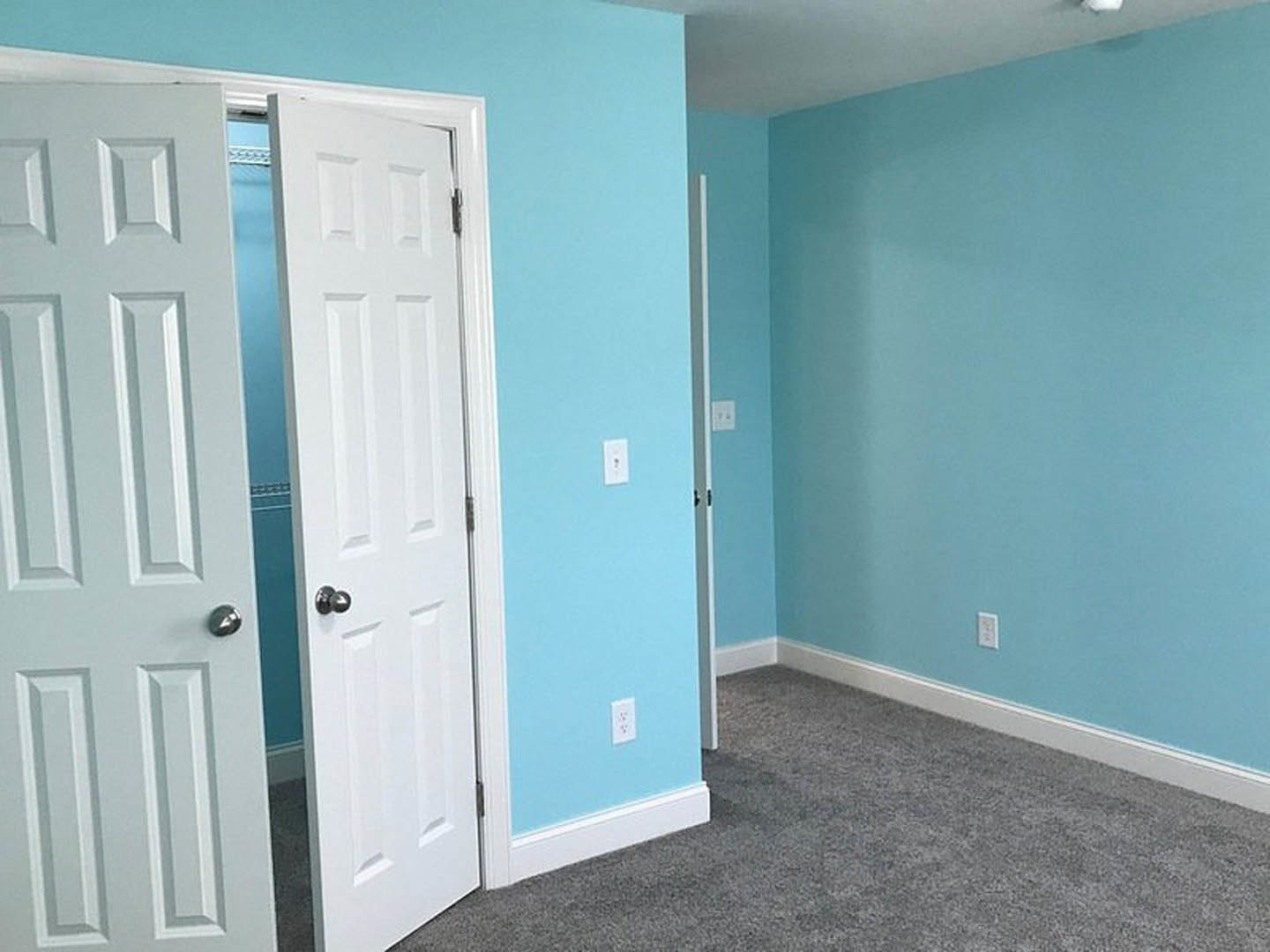 Blue-painted walls, white paneled doors with silver handles, grey carpet flooring, white ceiling, and plaster finishes