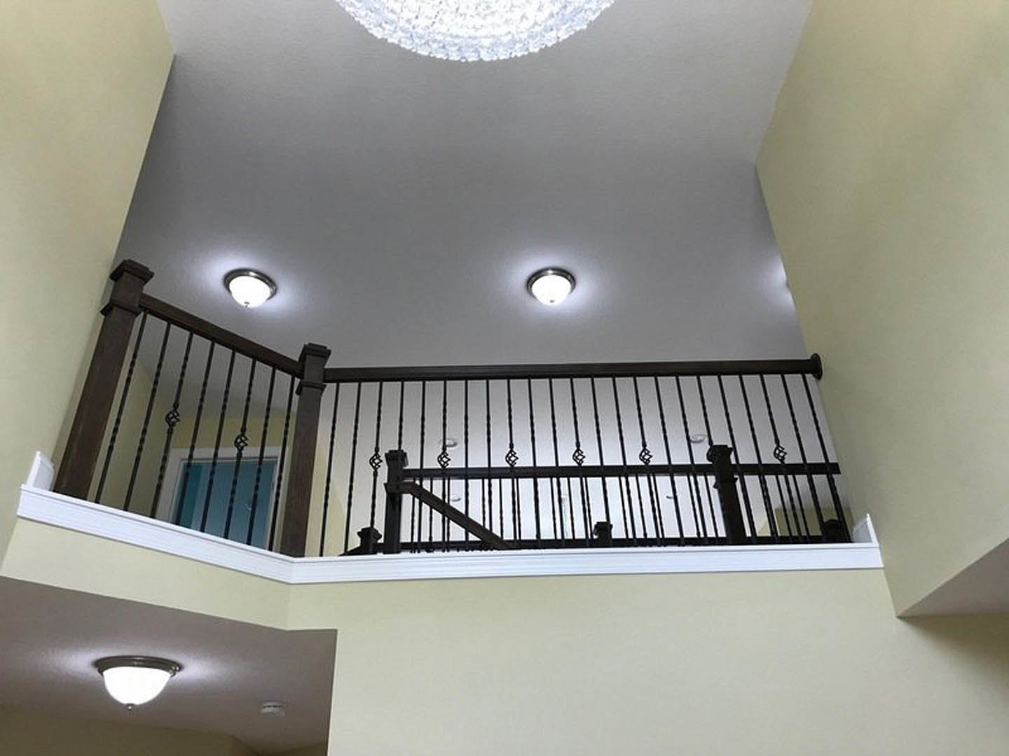 Staircase with matte black metal railing, white plaster walls, recessed ceiling light, and decorative molding
