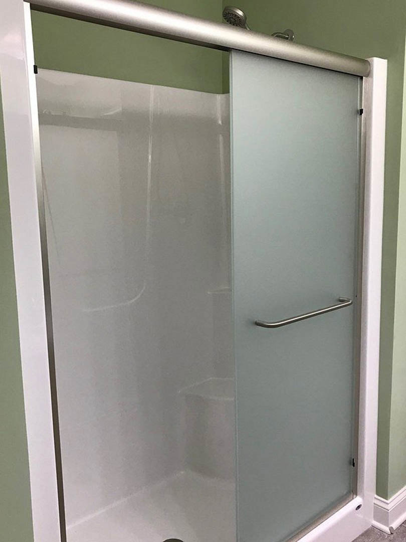Glass shower door with brushed metal handle, tiled bathroom walls, and chrome shower head visible through clear glass.