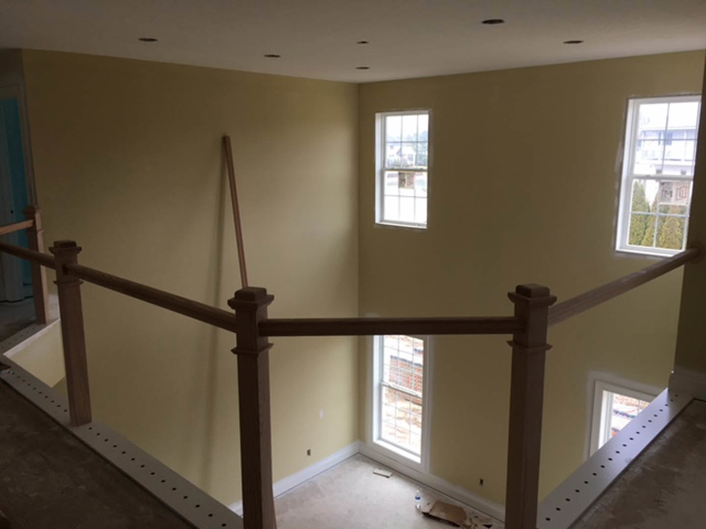 Open living area featuring a wooden staircase with metal railing, large windows allowing natural light, white plaster walls, hardwood flooring, and recessed ceiling lights.