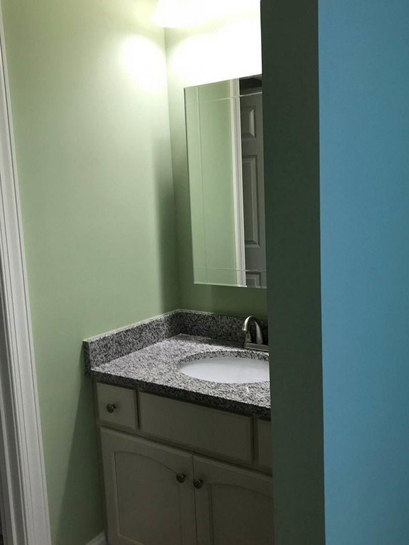 White bathroom vanity with undermount sink, chrome faucet, shaker-style cabinet, and rectangular mirror mounted above, set against light tile walls