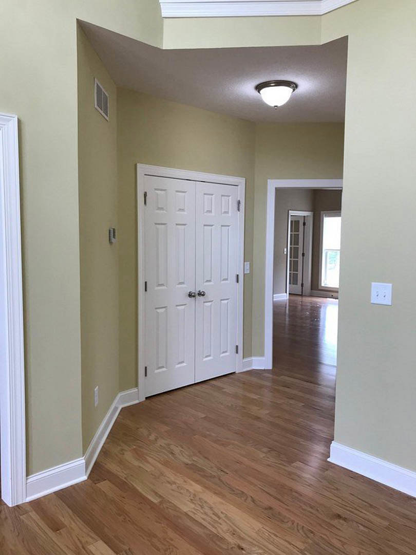 Hallway with white paneled doors, warm hardwood flooring, white walls, recessed ceiling light, and a glass door with white frame