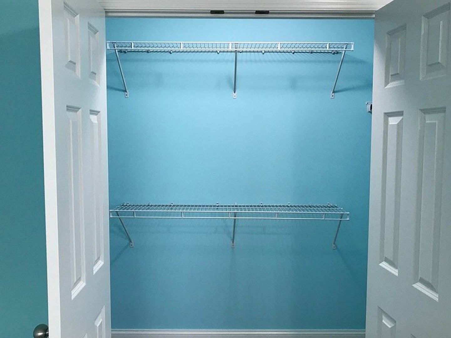 Open closet door revealing built-in white shelves, metal rod, and blue accent wall