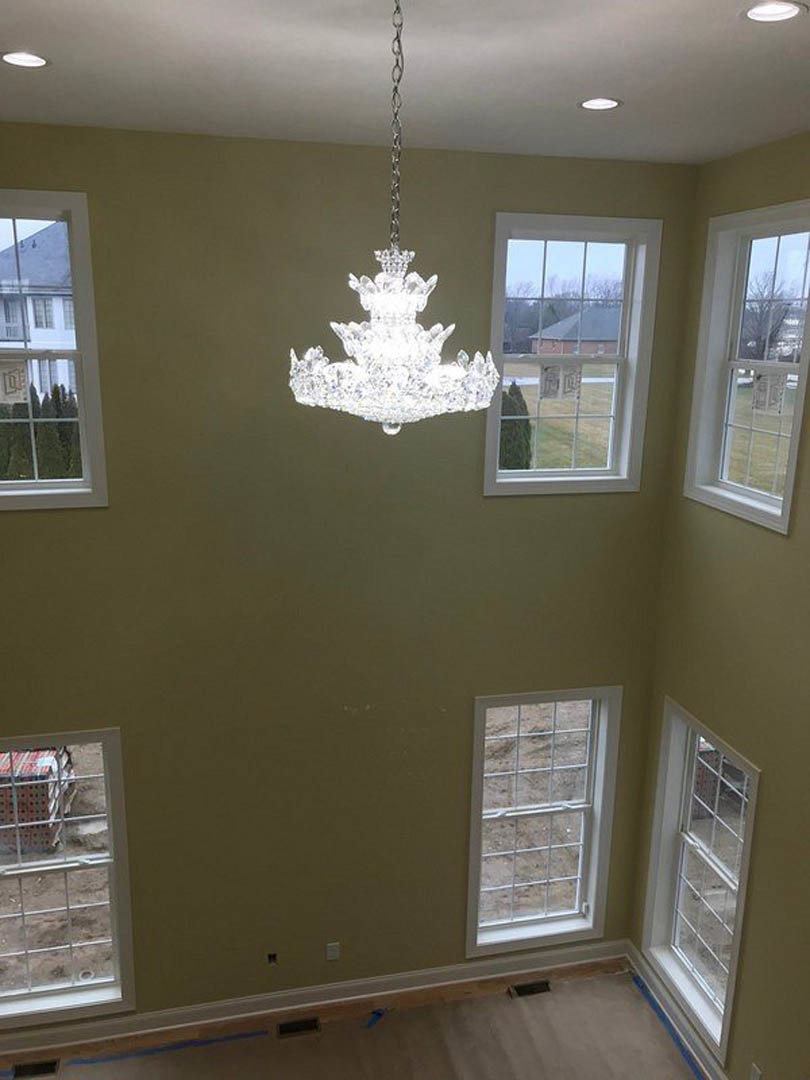 Crystal chandelier with tiered glass drops hanging from a white plaster ceiling, decorative crown molding, large window framing view of neighboring house.