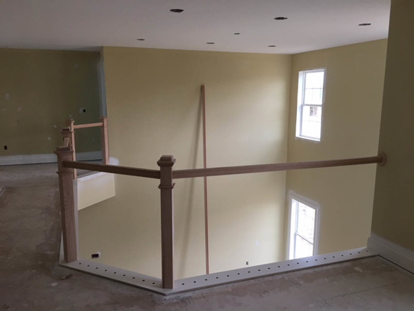 Wood railing along a plaster wall in a bright room with a white-framed window and light-colored flooring