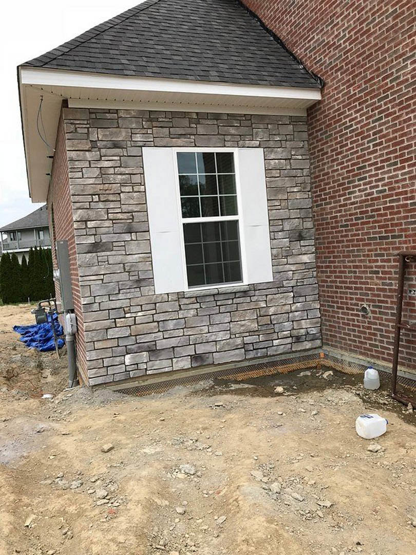 Red brick exterior wall with white-framed window, white plastic container on ground, trees in front of house
