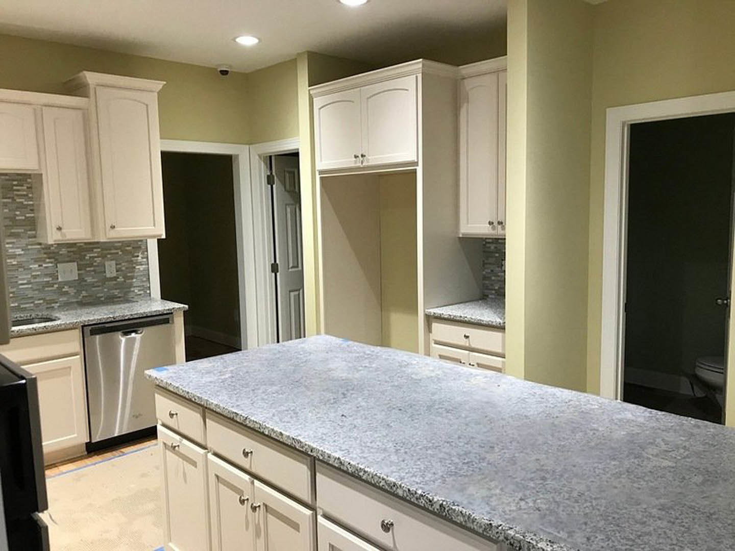 White kitchen cabinets with brushed nickel hardware, granite countertops, stainless steel dishwasher, undermount sink, and white tile backsplash.