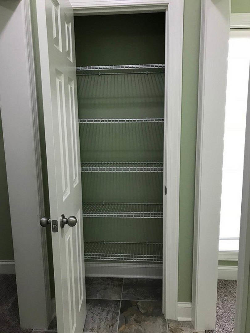 Walk-in closet with built-in white shelves, chrome door handle, and light tile flooring