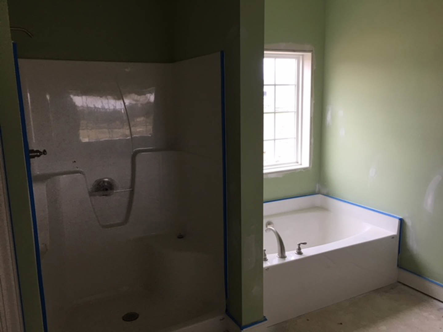 Bathroom with white tile walls, freestanding bathtub with chrome faucets, glass-enclosed shower, and large window letting in natural light.