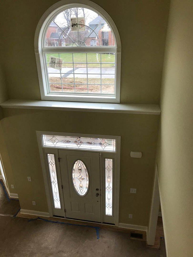 White door with a stained glass window above, paper taped to the window, surrounded by painted interior walls and flooring