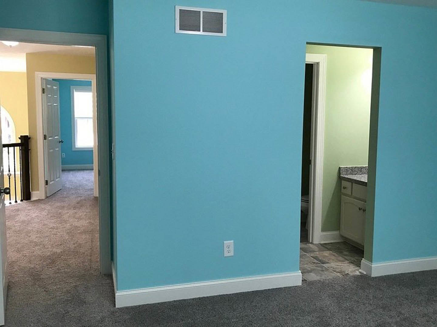 Blue painted wall with white electrical outlet, window trim, and door frame in a residential interior room; vent visible near floor.