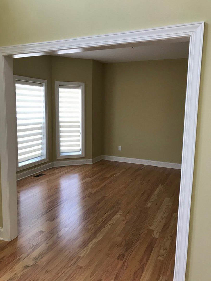 Wood floor room featuring white-framed windows with blinds, white door, and decorative white wall molding