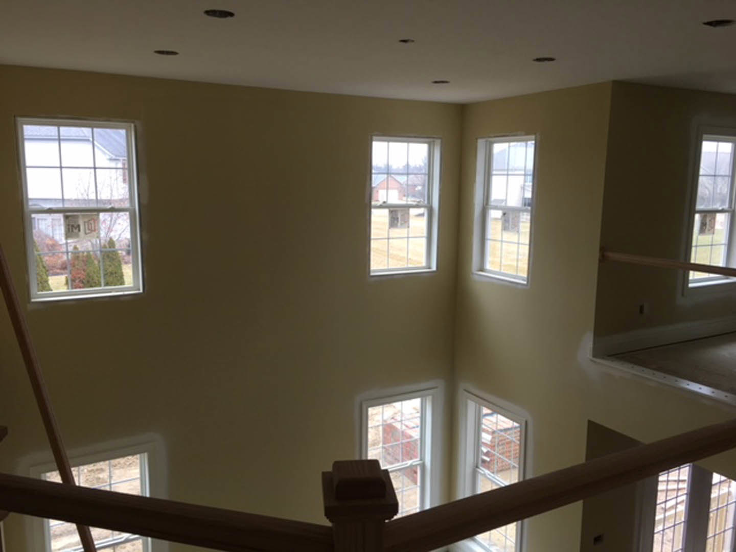Spacious room featuring multiple large windows, light plaster walls, hardwood floors, and a modern staircase with wooden posts.