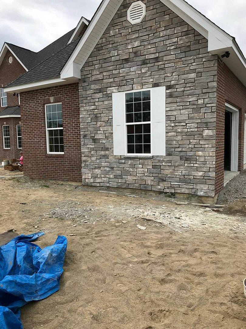 Red brick house exterior with multi-pane windows, white vent, and blue tarp spread across the ground