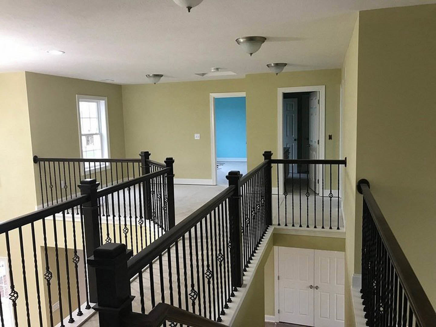 White double doors with silver knobs beside a staircase featuring black railings and balusters, white walls, window with white trim, and decorative molding.
