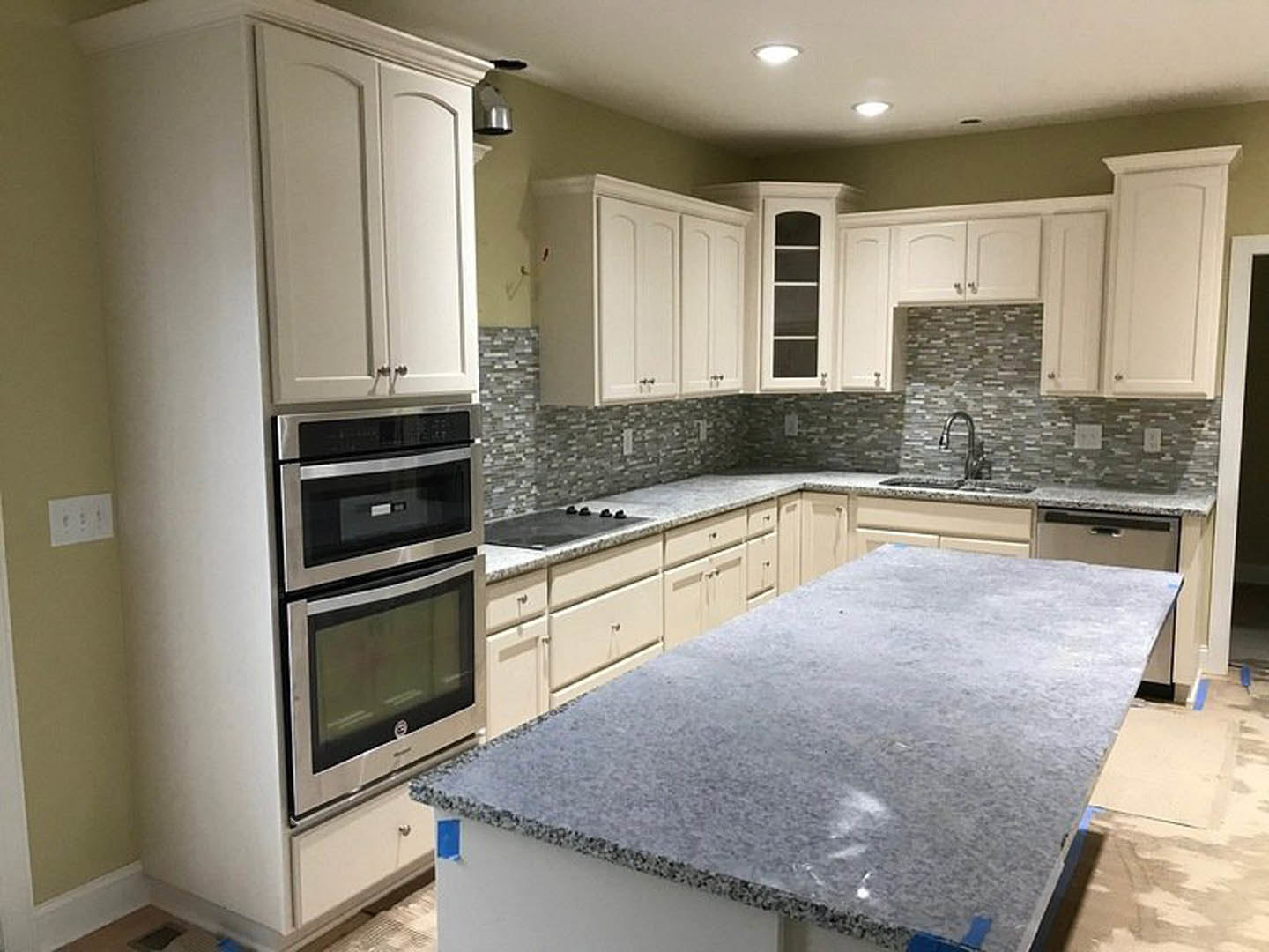 White kitchen cabinets and granite countertops, blue tape on counter, stainless steel microwave, white wall outlet with black buttons, window with white frame, close-up of lamp