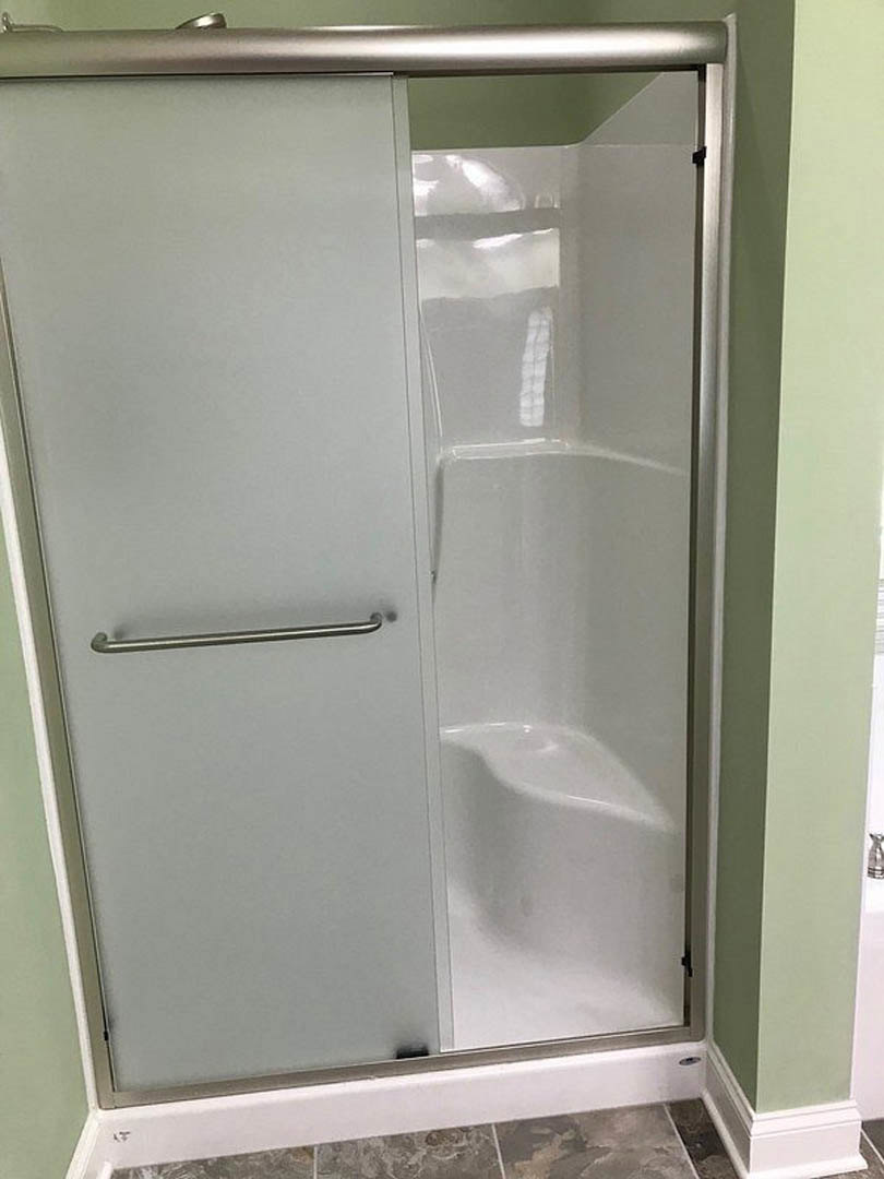 Glass shower enclosure with stone tile walls, white bathtub in the corner, and modern fixtures in a residential bathroom.