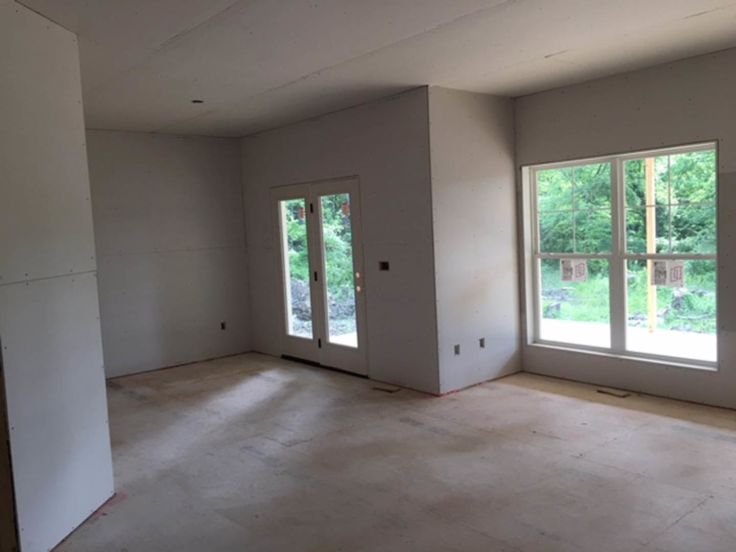 Spacious room featuring white-framed windows, glass doors, white flooring, and plaster walls with daylight streaming in