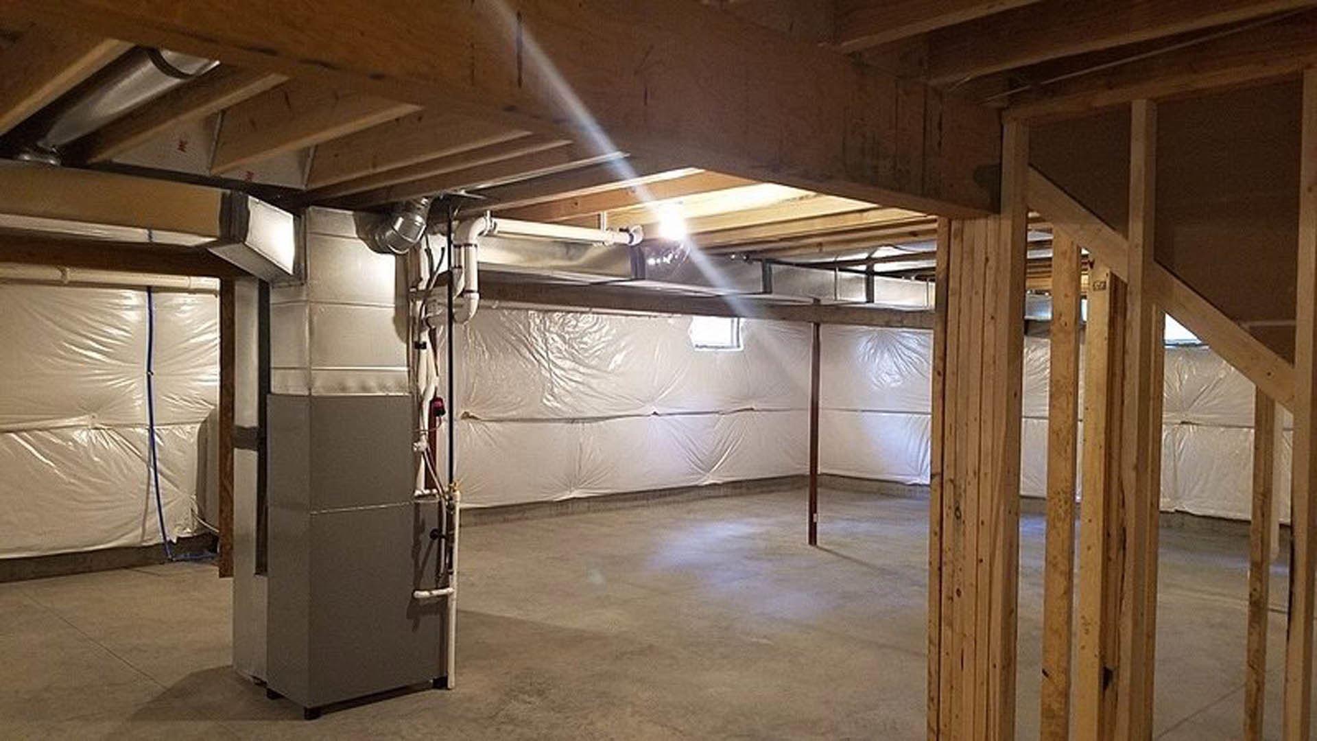 Room with white plaster walls, exposed wooden ceiling beams, concrete flooring, metal cabinet, and large white bag with blue hose.