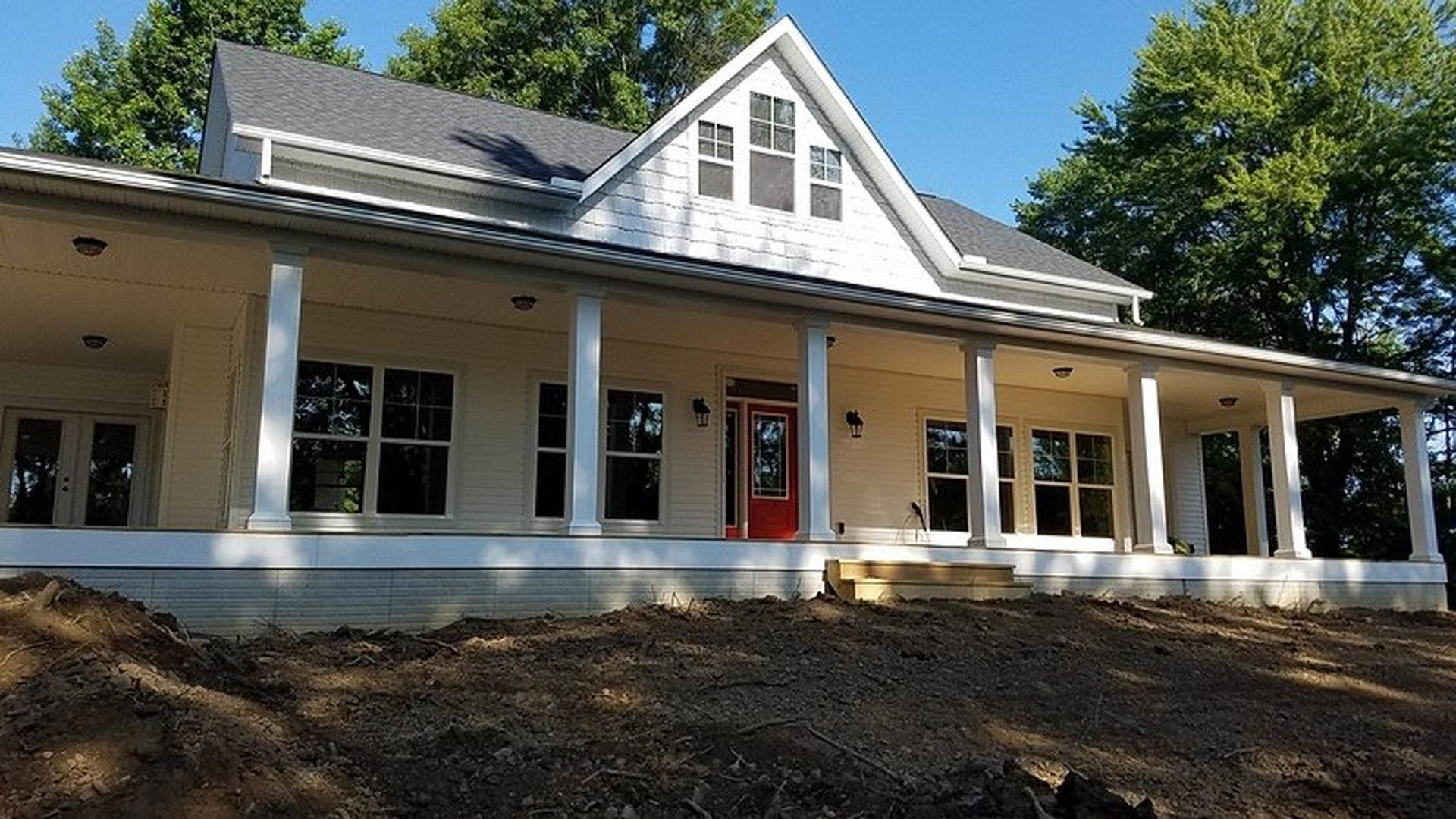 White house with columned porch, red front door, square-paned windows, and surrounding trees