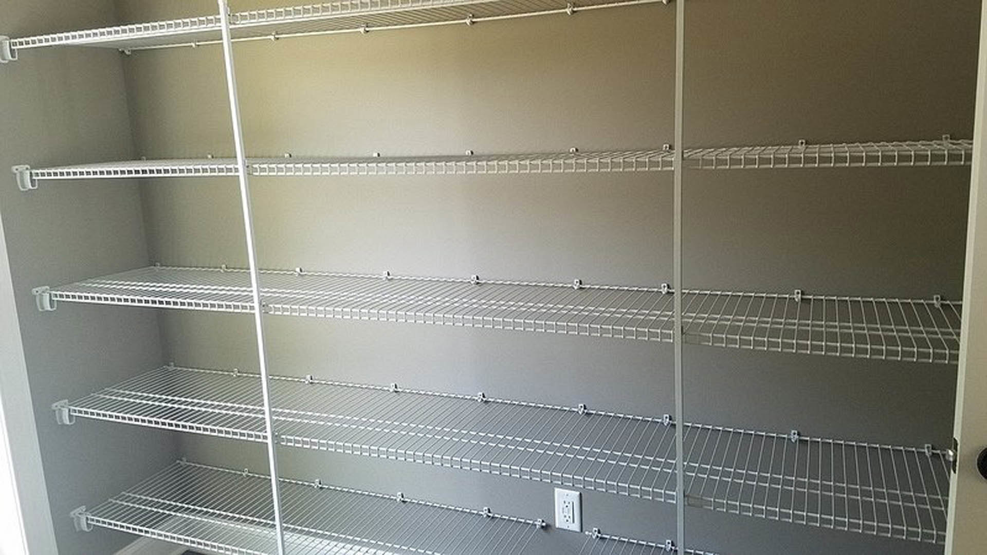 Closet interior featuring built-in white shelves and a wall-mounted power outlet