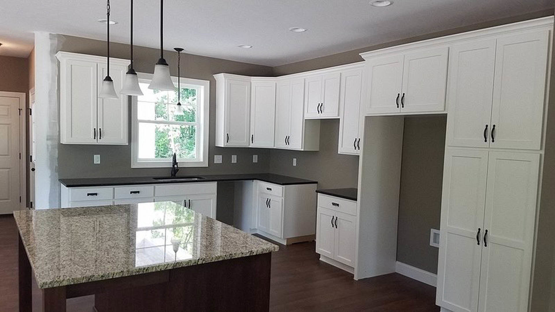 White kitchen cabinets, marble countertop with under-cabinet lighting, stainless steel sink, modern appliances, and light-colored walls