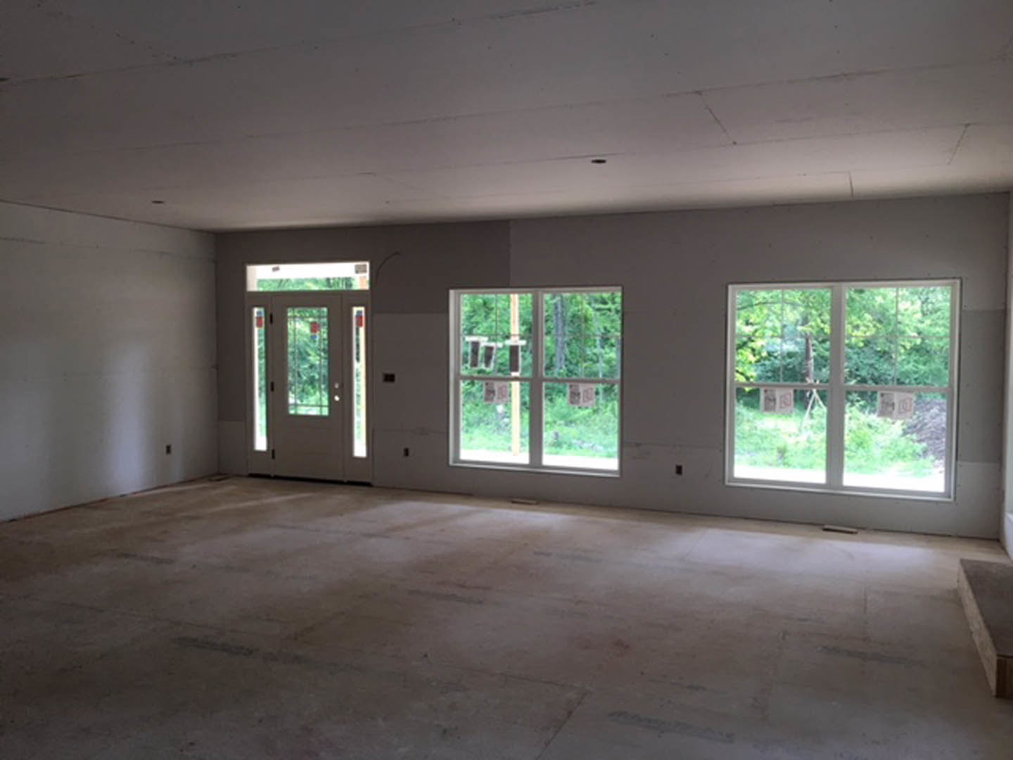 Spacious room featuring white-framed windows, glass-paneled door, light wood flooring, and neutral walls with natural daylight illuminating the interior.