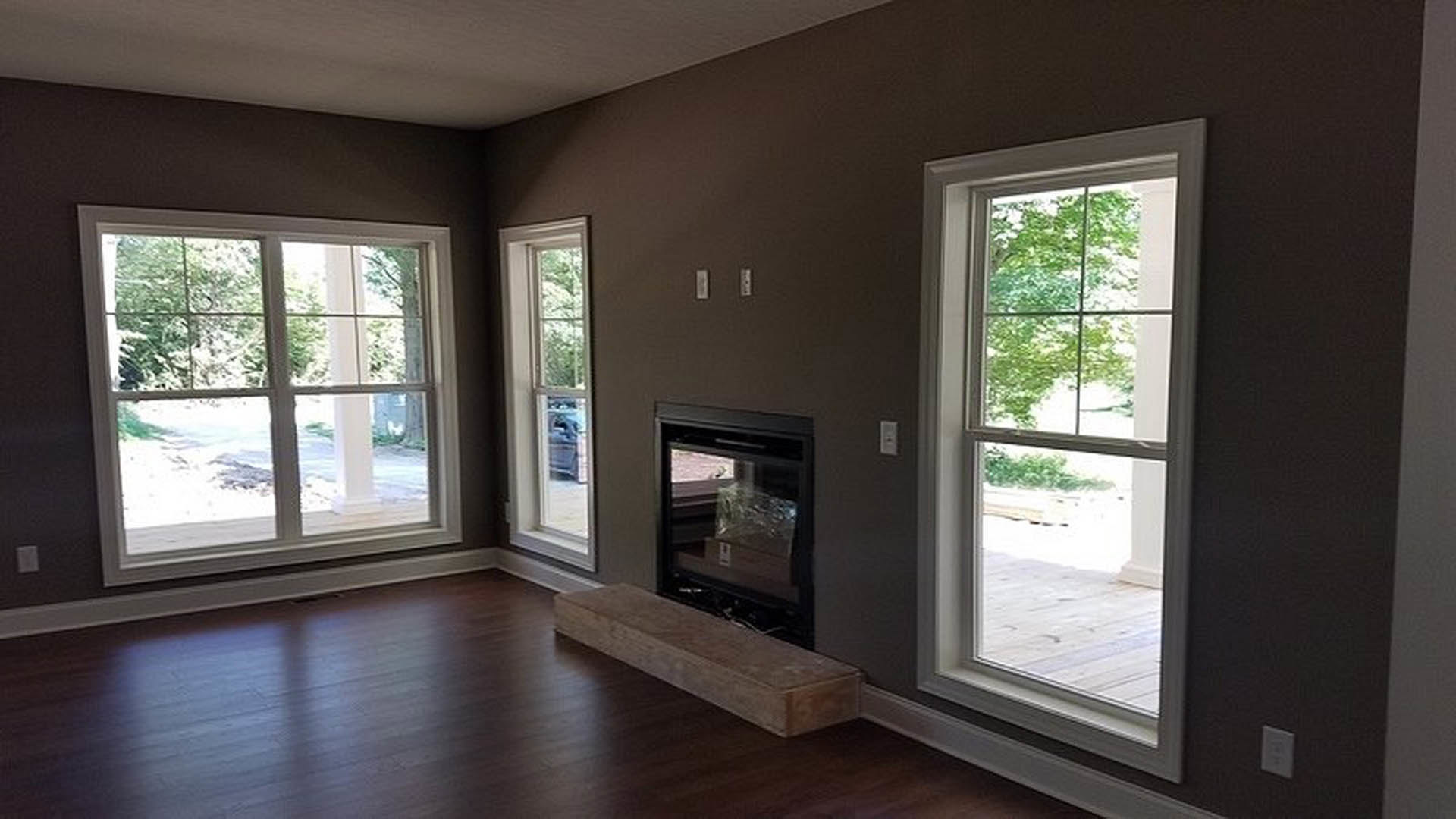 Living room with laminate flooring, white walls, central stone fireplace, large windows letting in natural light, and minimal modern decor.