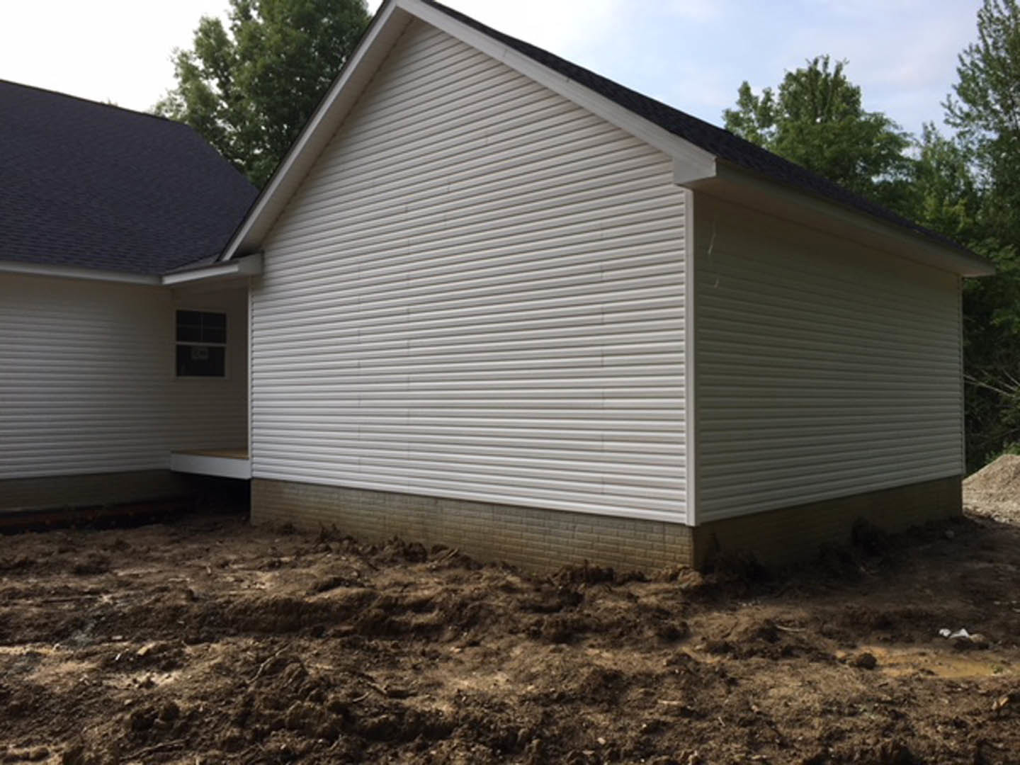 White house with black roof, white-framed window, dirt yard in foreground, trees and sky in background
