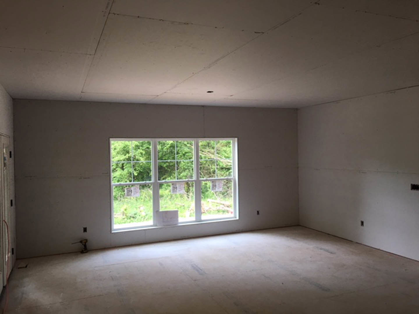Sunlit room featuring a large window with white frames, smooth concrete flooring, plaster walls, and views of trees outside.