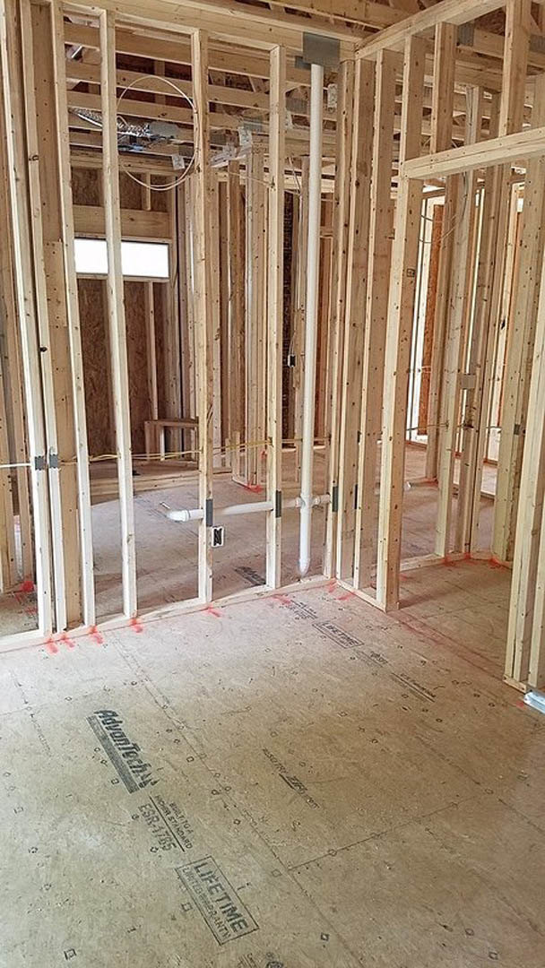 Wood-framed room under construction with exposed beams, concrete floor, and visible insulation panels