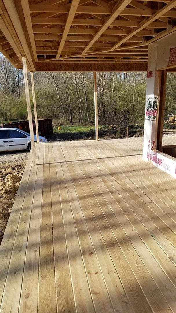 Wood deck with exposed wooden beams and roof, white structural supports, white car parked beside the road, shaded outdoor porch area.