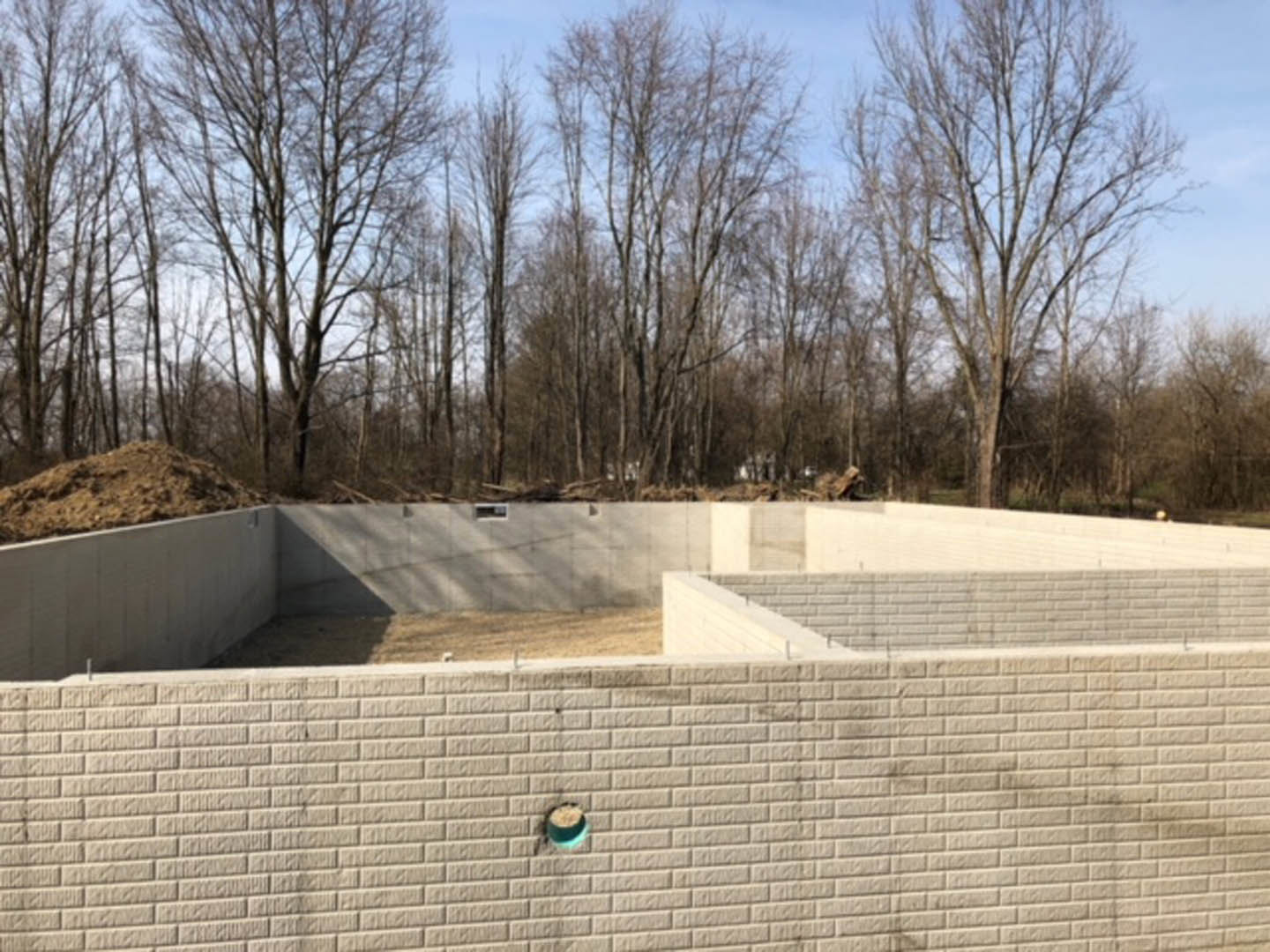 Concrete foundation slab surrounded by leafy trees, exposed soil, and clear sky in the background