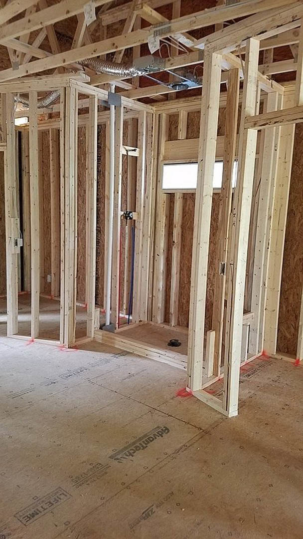 Exposed wood framing with vertical and horizontal beams, unfinished floor, visible metal pipe, and white rectangular insulation panel.