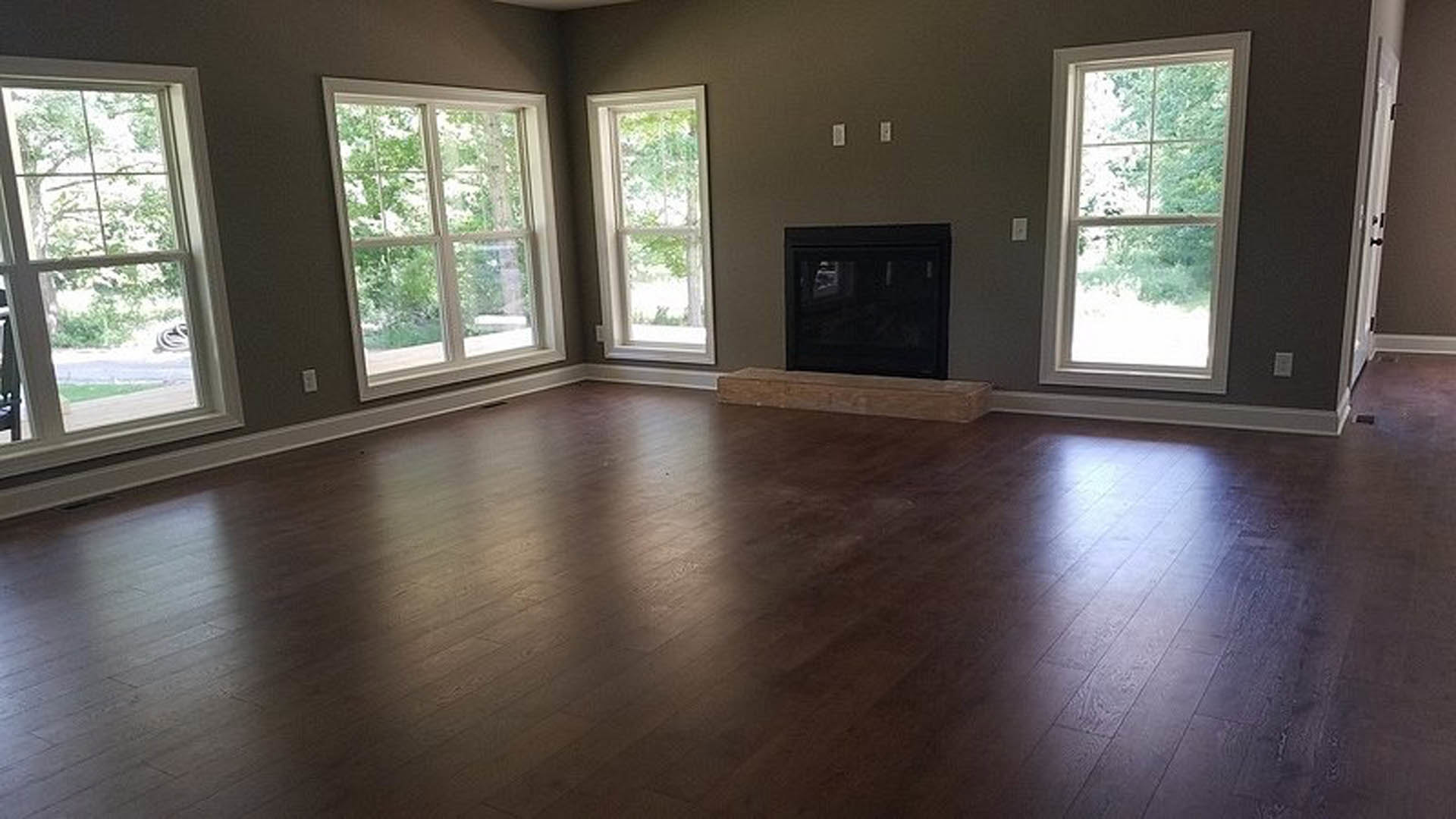 Living room with hardwood floors, modern black fireplace with glass front, large windows overlooking trees, white walls, and natural wood finishes