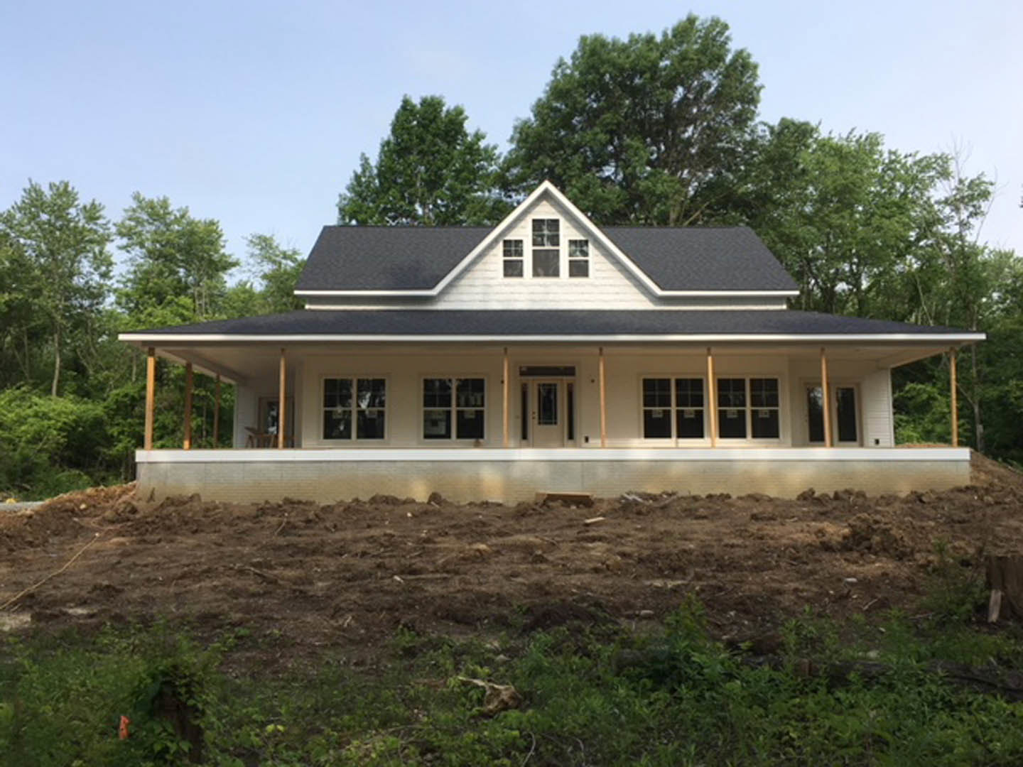 White house with prominent triangular roof, spacious front porch with white columns, large windows, grassy yard, and mature trees in background