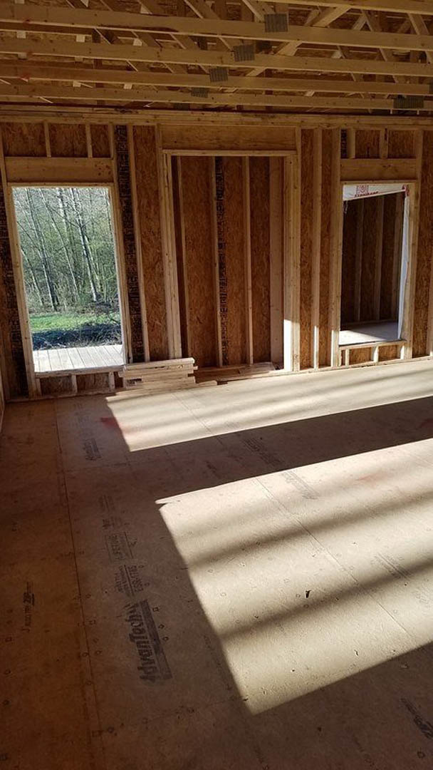 Hardwood floor with small holes, wooden ceiling beams, large windows, and a single door in a bright interior room