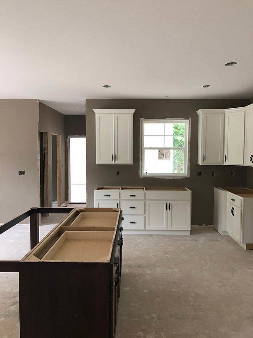 White kitchen with shaker cabinets and black handles, wood shelf on island, light fixture near window, dining table adjacent to workspace.