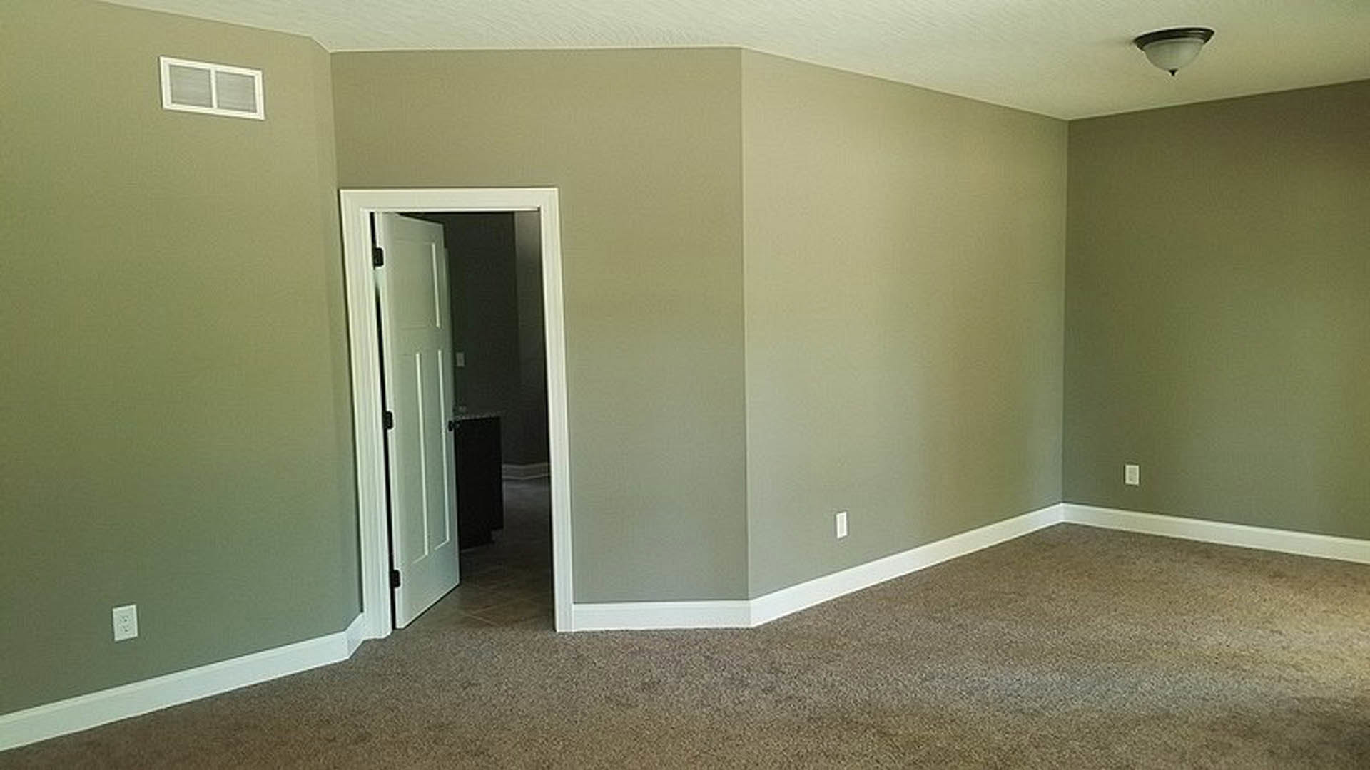 Open door leading into a room with light-colored plaster walls, white square window with matching frame, white electrical outlet, and neutral flooring