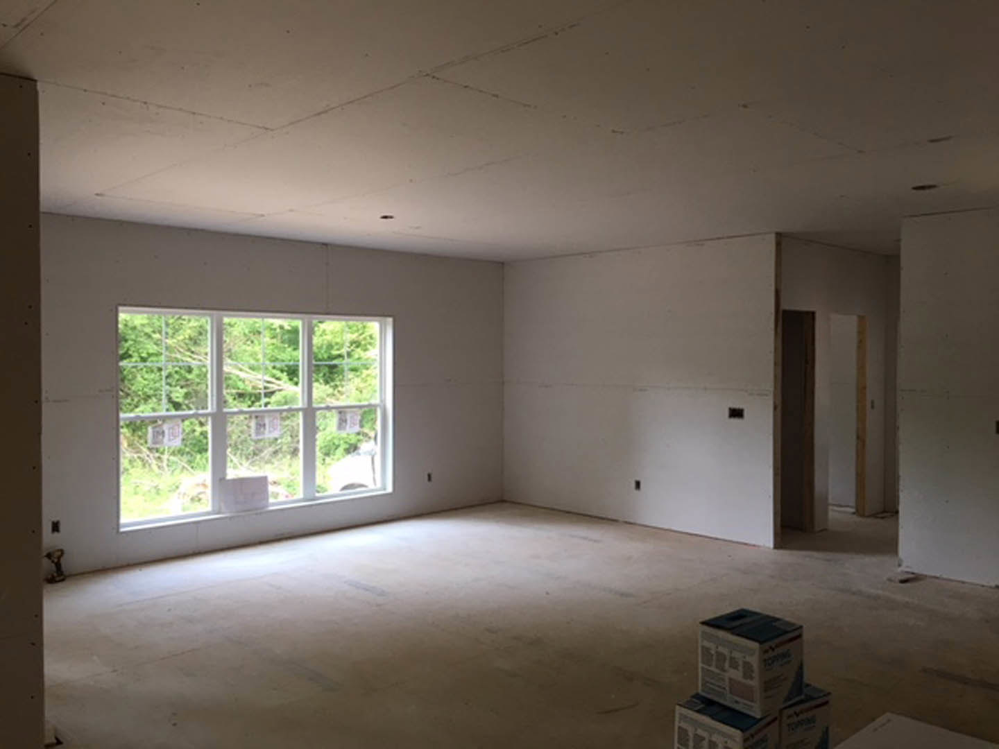 Bright room with white plaster walls, black-framed window displaying multiple signs, stack of cardboard boxes on a table, light-colored flooring