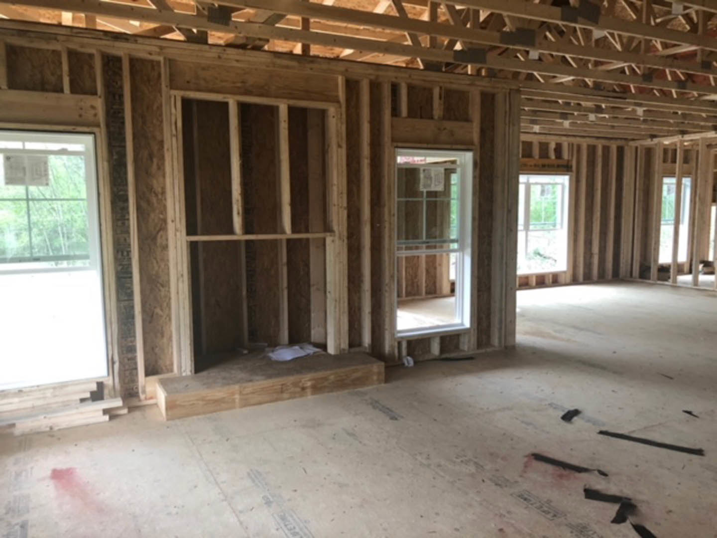White-framed window with tree views, wooden door, exposed ceiling beams, light wood flooring, and neutral walls