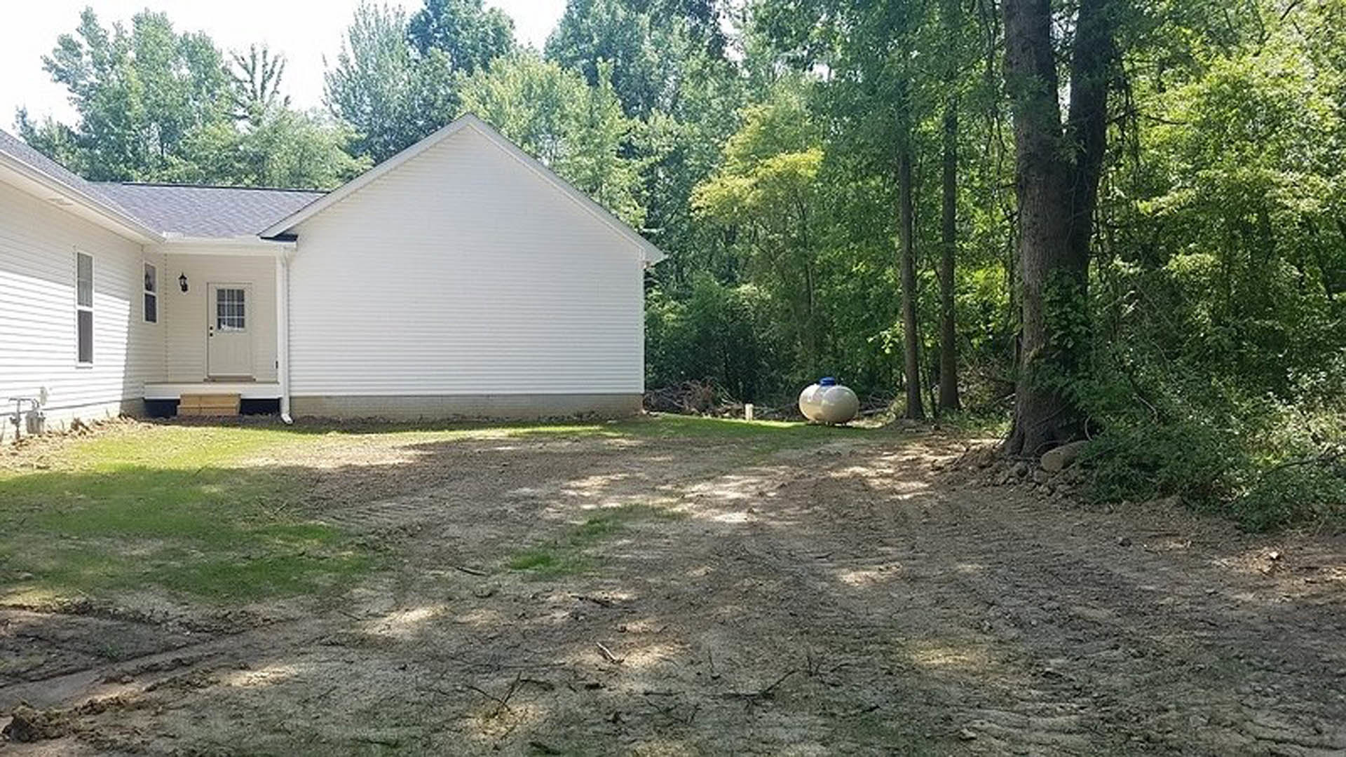 White cottage-style home with multi-pane windows, white door with glass insert, and a large spherical white sculpture centered on a dirt and grassy yard surrounded by scattered