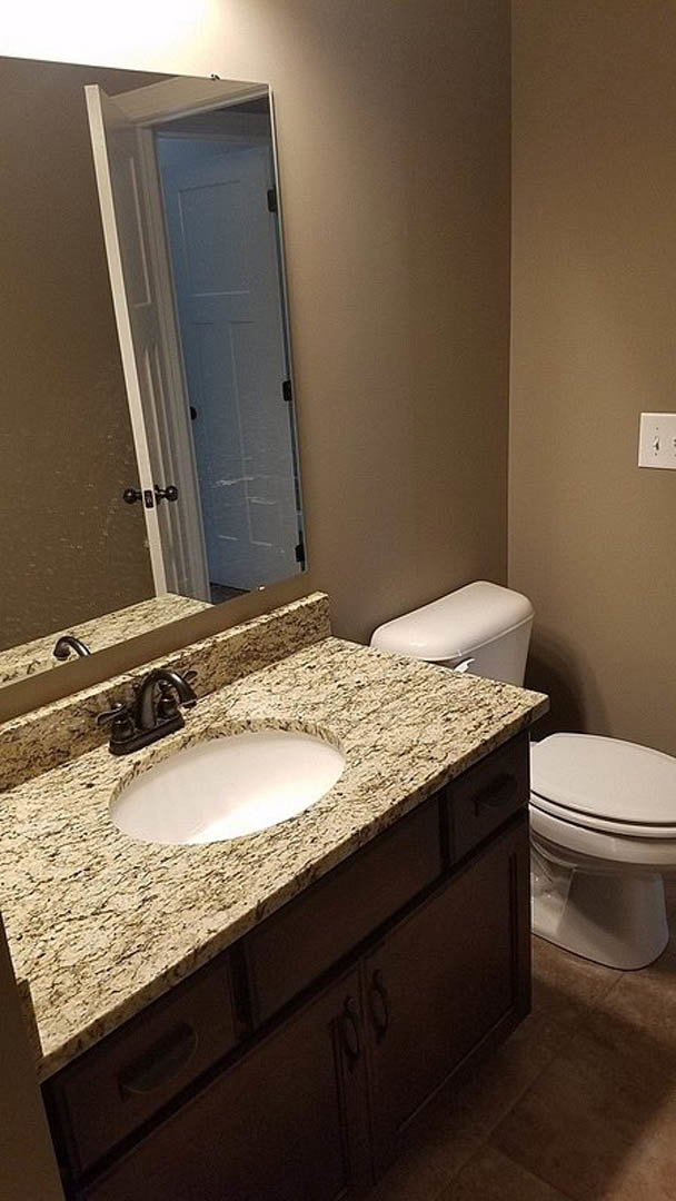 Bathroom featuring a marble countertop sink, white toilet, tiled walls, and chrome faucet