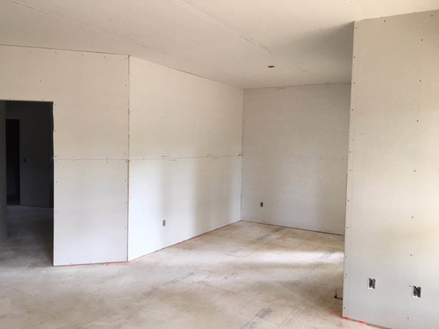 Modern room featuring smooth white walls, exposed concrete flooring, and a minimalist door with clean lines