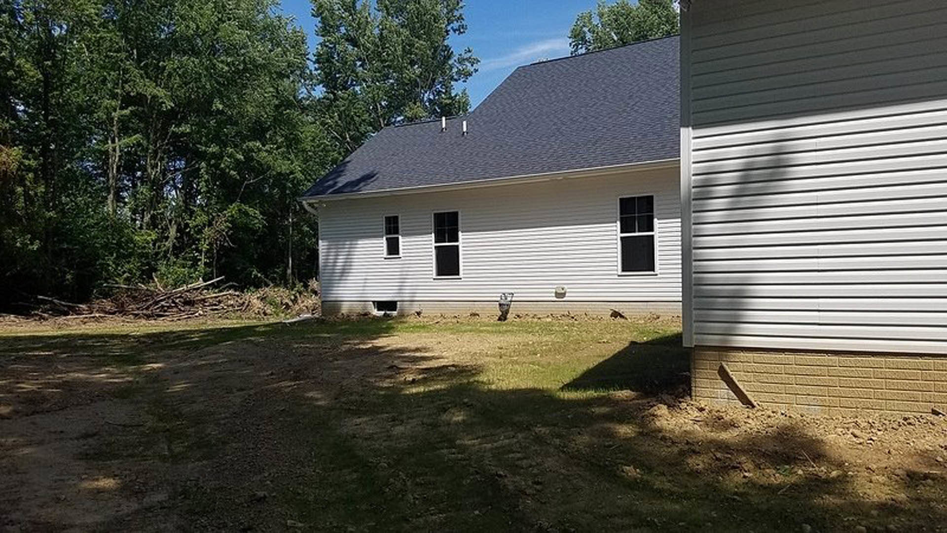 Two-story home with light siding, white-framed windows, grassy yard, and tree casting shadow on exterior wall
